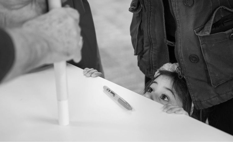 Black and white photograph of a young girl looking up at someone demonstrating how to make a paper rocket